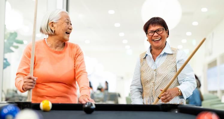 Two elderly women enjoy playing a game of billiards