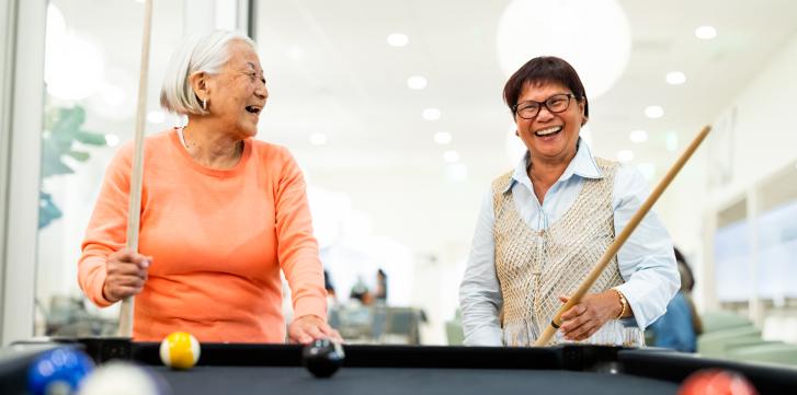 Two elderly women enjoy playing a game of billiards
